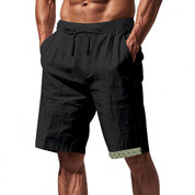 Pantaloncini uomo neri con elastico in vita e tasche, dettagli geometrici verdi sull'orlo. Ideali per sport e tempo libero.