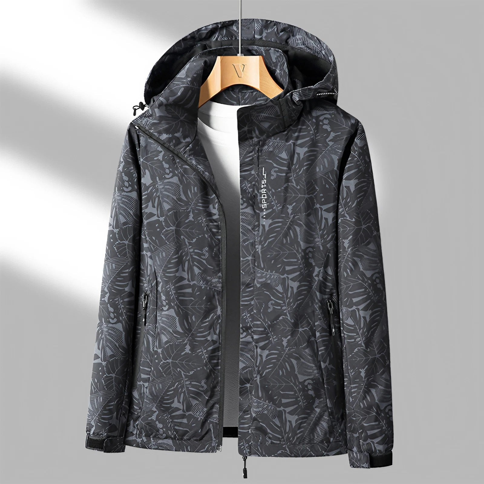 Giacca a vento impermeabile nera con motivo foglie, cappuccio regolabile, zip frontale, ideale per attività outdoor. Disponibile su appendiabiti.