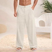Pantaloni larghi da uomo in lino bianco, stile casual estivo, con tasche laterali. Indossati con sandali, ambientazione interna moderna.