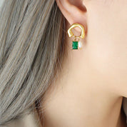Orecchino dorato con pendente verde smeraldo e perla su orecchio femminile, gioielli eleganti, accessori moda donna, stile moderno.