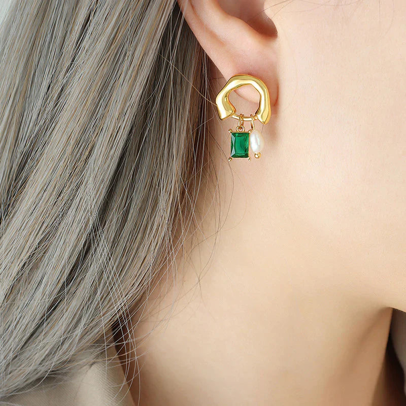 Orecchino dorato con pendente verde smeraldo e perla su orecchio femminile, gioielli eleganti, accessori moda donna, stile moderno.