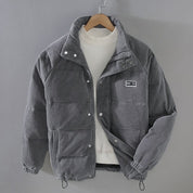 Giacca invernale grigia in velluto a coste, con colletto alto e chiusura a bottoni, appesa su gruccia. Design casual, ideale per moda uomo.