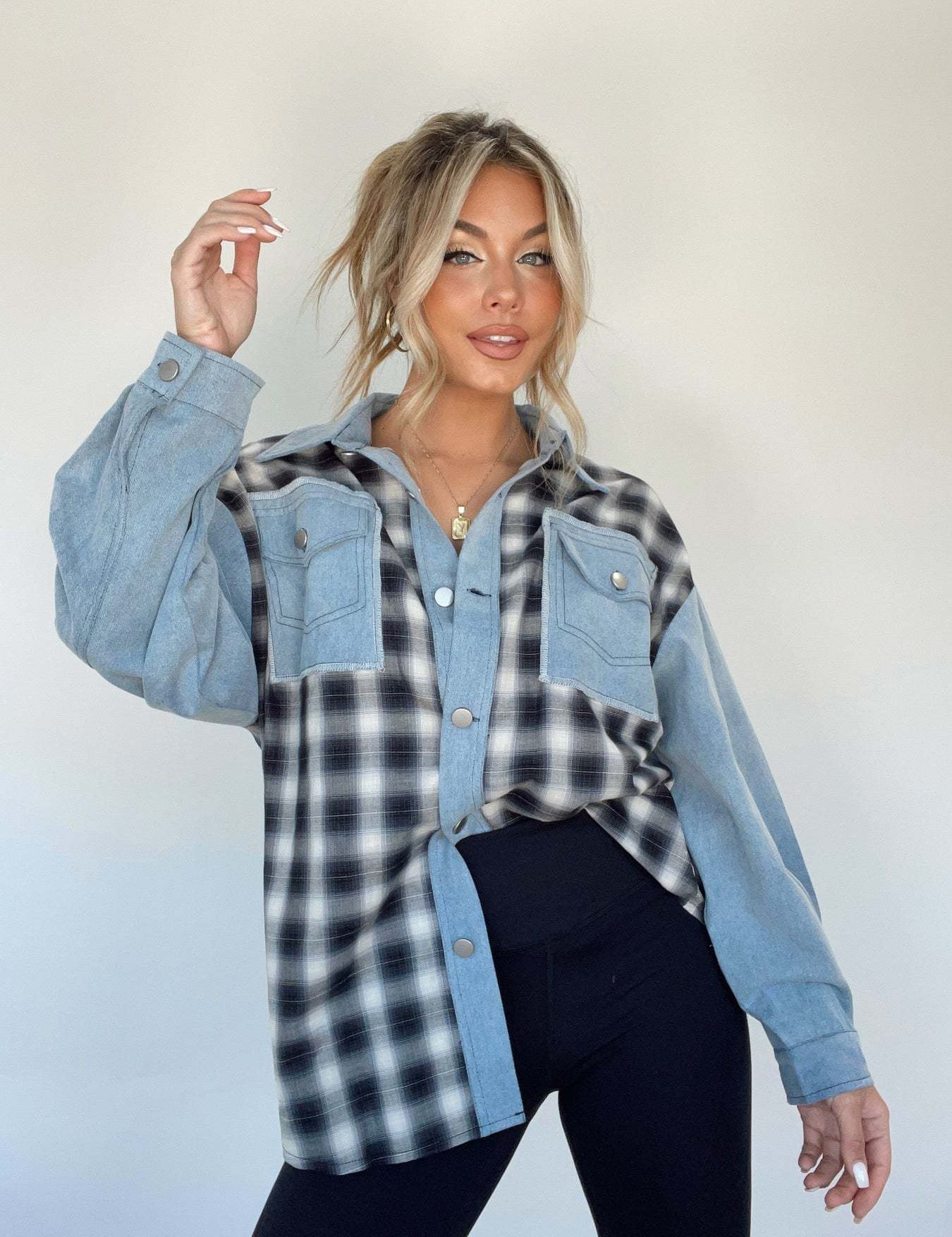 Donna con camicia a quadri bianca e nera, maniche in denim, posa su sfondo neutro. Moda casual, stile autunnale, abbigliamento femminile trendy.
