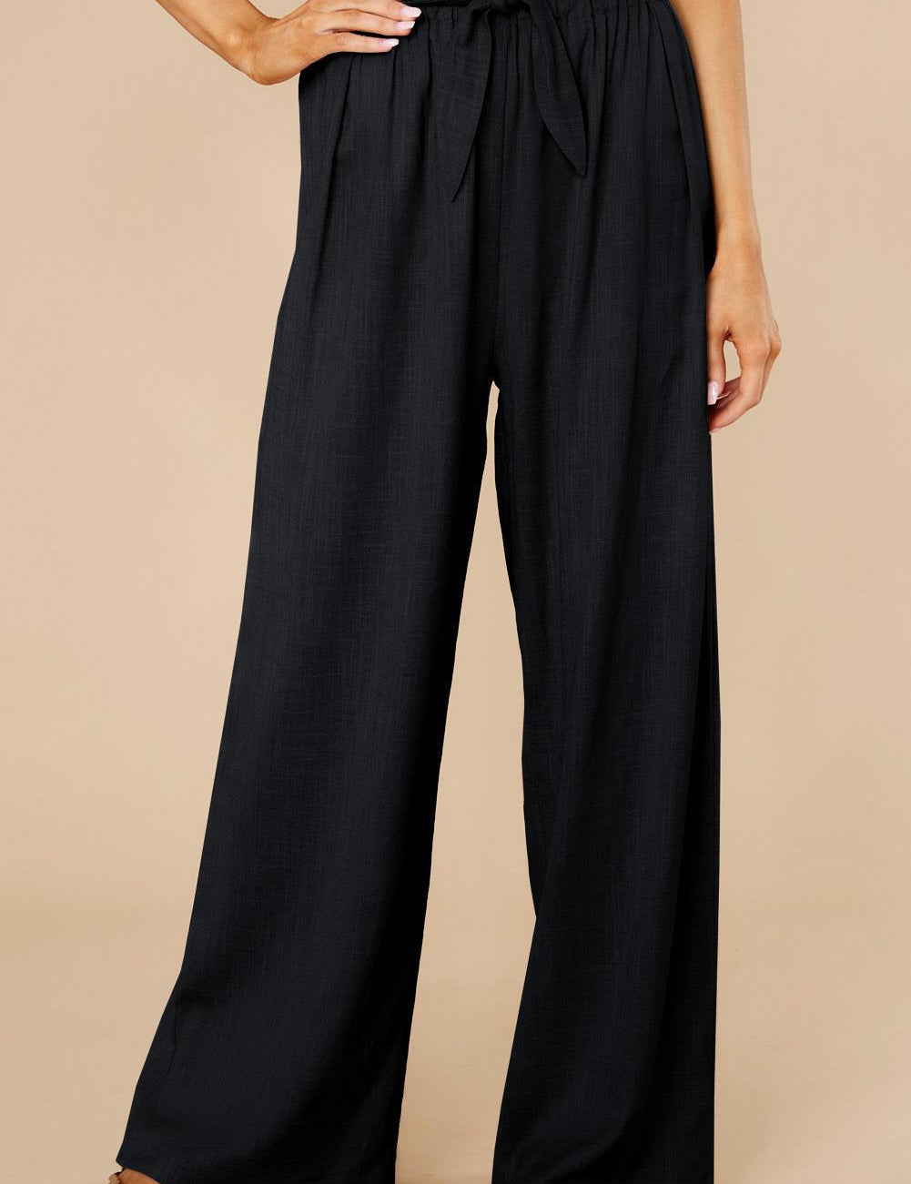 Pantaloni neri a vita alta con cintura, design ampio e pieghe, indossati da una modella. Ideali per look eleganti e casual.