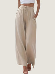 Pantaloni palazzo beige da donna, vita alta con coulisse, tessuto leggero, tasche laterali, abbinati a top bianco. Moda estiva casual elegante.