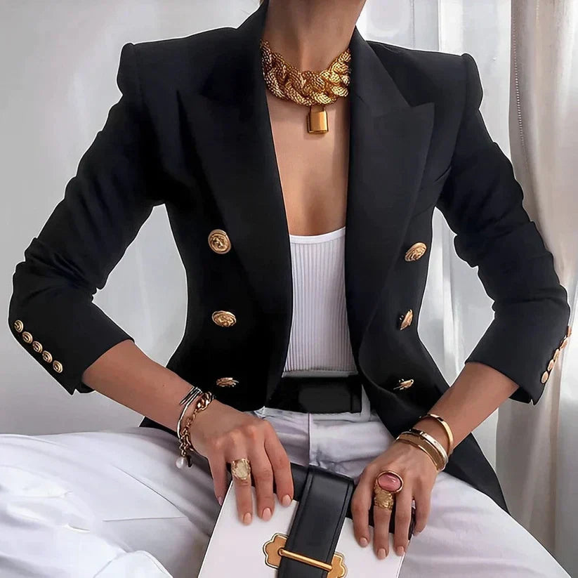 Giacca nera elegante con bottoni dorati, indossata su top bianco. Accessori: collana dorata, anelli, bracciali. Look sofisticato e moderno.