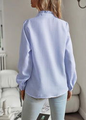 Donna con camicia a maniche lunghe azzurra, tessuto a trama leggera, in un ambiente interno moderno. Moda femminile, abbigliamento casual elegante.