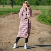 Donna con cappotto lungo a maglia rosa, cappuccio, su strada sterrata. Moda autunnale, abbigliamento casual, stile confortevole.