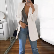 Donna in blazer bianco e jeans, specchio, camera da letto moderna, moda casual chic, outfit elegante, borsa a tracolla nera, stile contemporaneo.