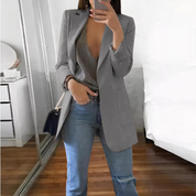 Donna con blazer grigio elegante, jeans casual, top scollato, specchio, camera da letto moderna. Moda femminile, abbigliamento casual chic.