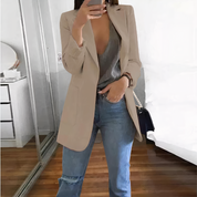 Donna con blazer beige, top grigio e jeans strappati, specchio sullo sfondo. Moda casual chic, outfit autunnale, stile urbano elegante.