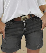 Shorts di jeans neri con bottoni, cintura con fibbia ovale, indossati con maglietta bianca. Moda casual estiva, abbigliamento donna trendy.