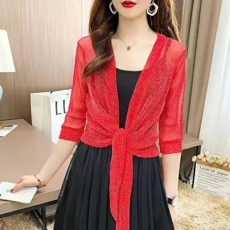 Donna con cardigan rosso trasparente annodato, abito nero elegante, orecchini a cerchio, in un ambiente moderno. Moda femminile, abbigliamento elegante.