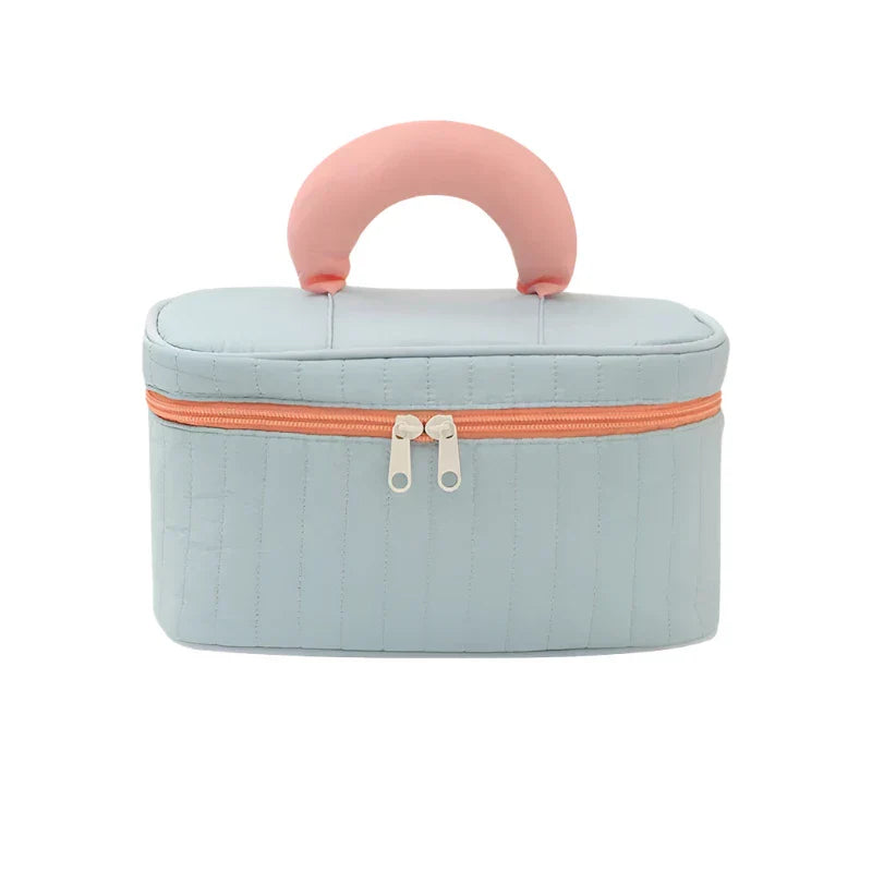 Astuccio cosmetico portatile in tessuto trapuntato azzurro con manico rosa, chiusura a zip arancione. Ideale per viaggi e organizzazione trucco.