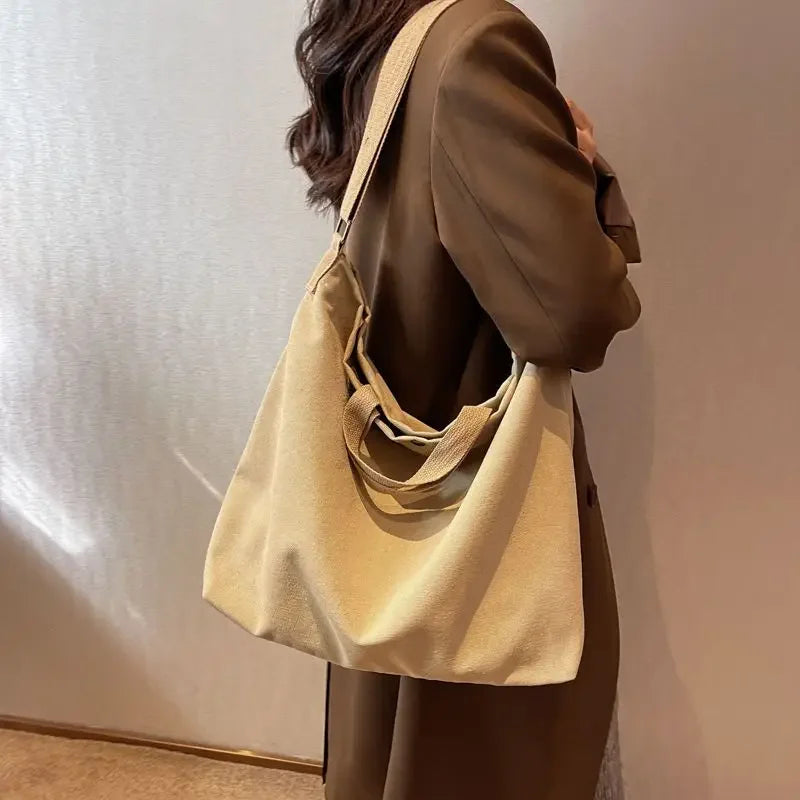 Donna con cappotto marrone indossa borsa a tracolla beige in tessuto, elegante e spaziosa, perfetta per moda autunnale e shopping quotidiano.