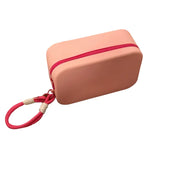 Custodia rosa in silicone con cerniera rossa e cinturino, ideale per protezione e trasporto di piccoli oggetti. Design compatto e resistente.