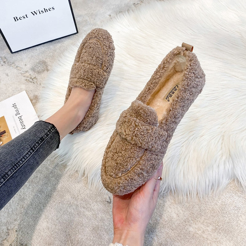 Scarpe mocassini in pelliccia sintetica marrone, comode e calde, su tappeto bianco. Ideali per l'inverno, moda donna, stile casual.
