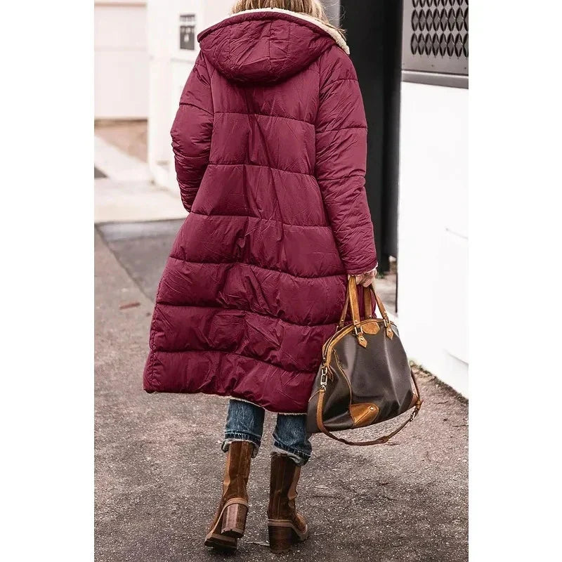 Donna con cappotto lungo imbottito bordeaux, jeans e stivali marroni, borsa a mano in pelle. Moda invernale, abbigliamento caldo e casual.