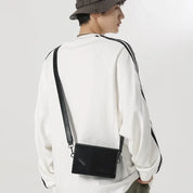 Giovane con borsa a tracolla nera in pelle, indossa maglia bianca e cappello. Moda casual uomo, accessori eleganti, stile urbano.