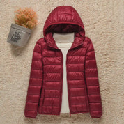 Giacca invernale donna rossa con cappuccio, imbottita, su sfondo beige. Moda calda e casual, perfetta per l'autunno e l'inverno.