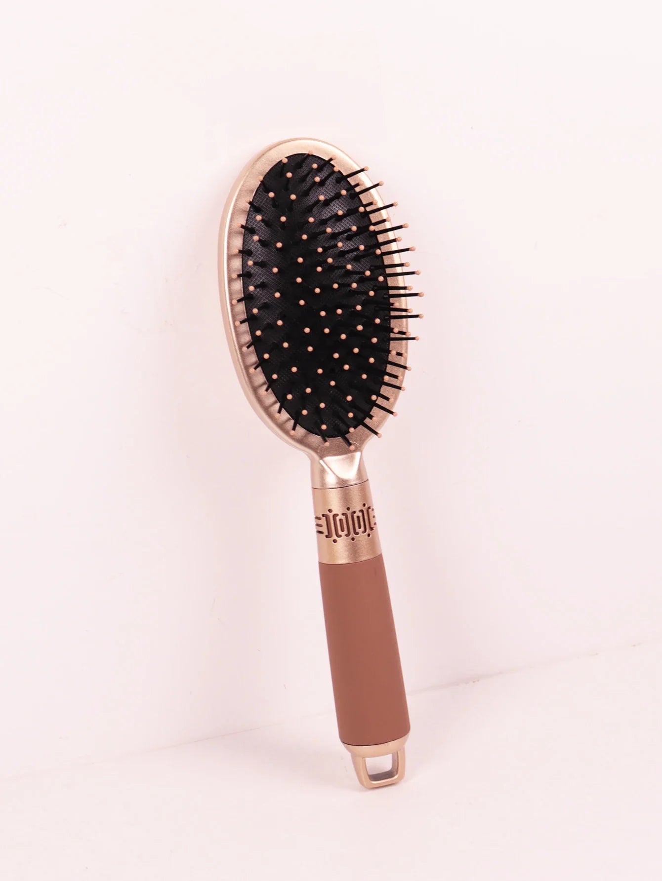 Spazzola per capelli ovale con setole nere e punte dorate, manico ergonomico marrone. Accessorio styling capelli, ideale per districare e lisciare.