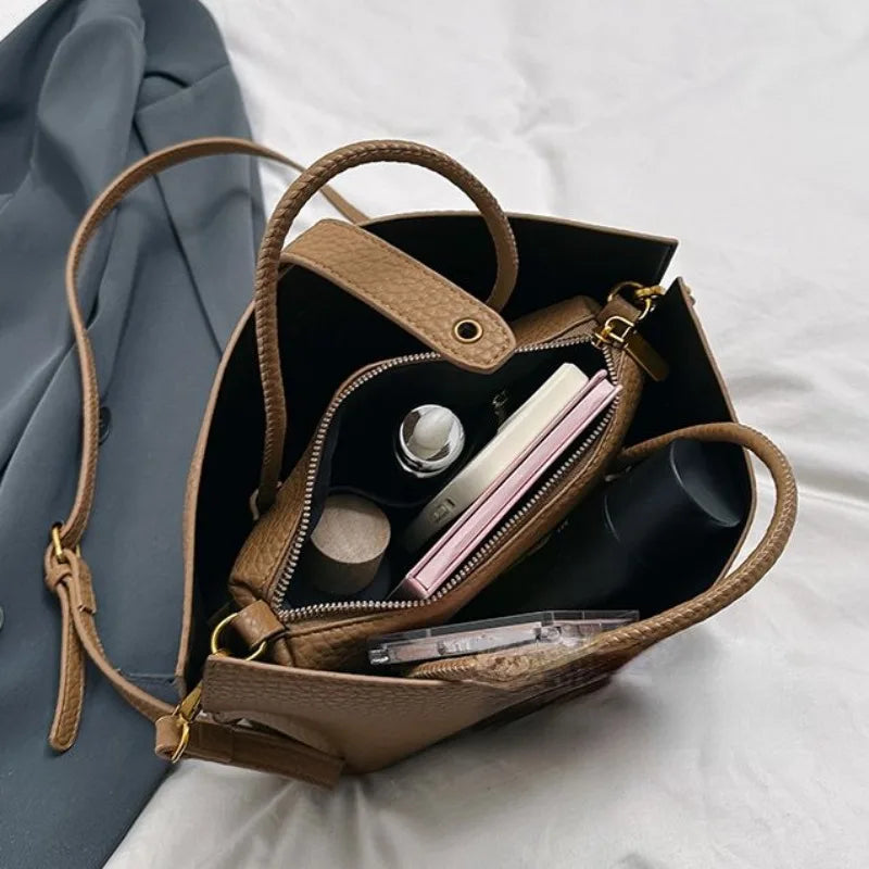 Borsa a tracolla marrone in pelle con oggetti personali all'interno, tra cui portafoglio, bottiglia e cosmetici, su sfondo bianco. Accessori moda donna.