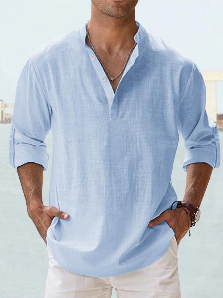 Camicia uomo in lino azzurro, maniche lunghe arrotolate, colletto alla coreana, abbinata a pantaloni bianchi. Stile casual estivo elegante.