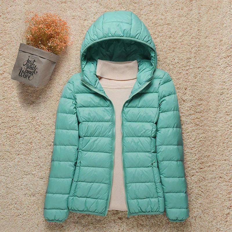 Giacca invernale verde acqua con cappuccio, imbottita, su sfondo beige. Moda donna, abbigliamento caldo, stile casual.