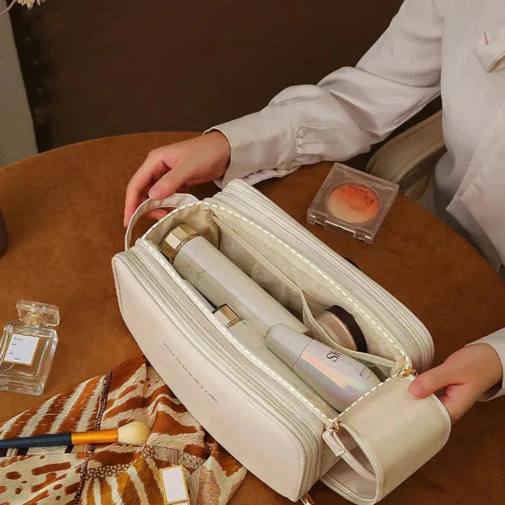 Borsa cosmetica beige su tavolo con trucco e profumo, contenente prodotti di bellezza. Ideale per organizzare accessori cosmetici da viaggio.