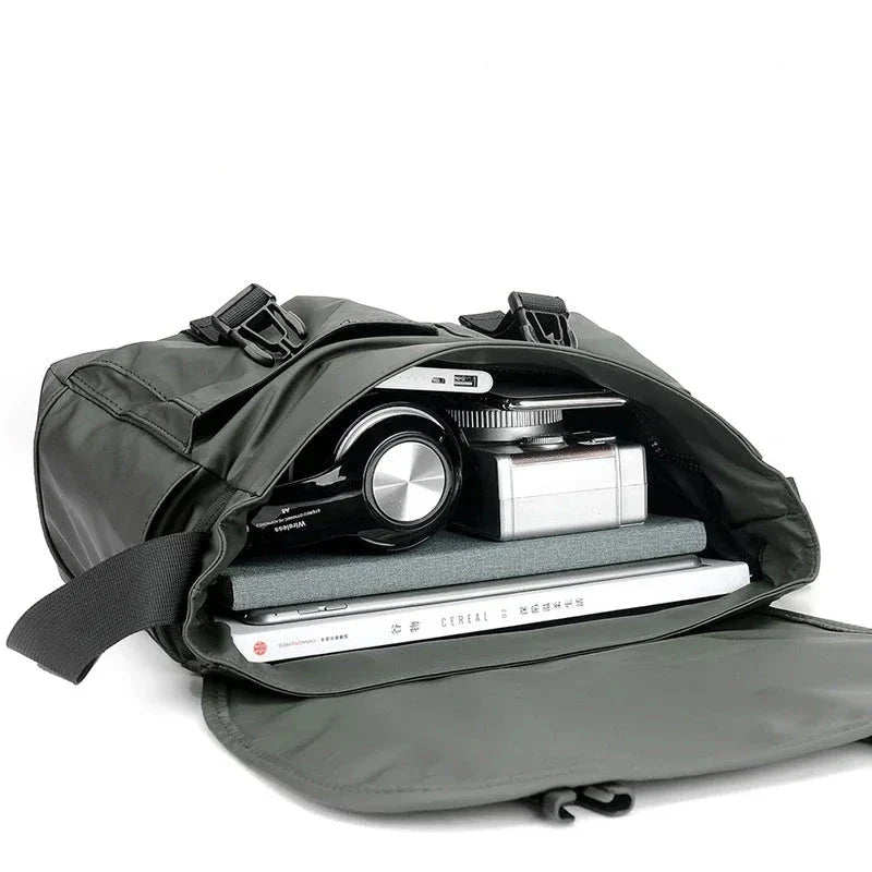 Borsa a tracolla verde aperta con fotocamera, libri e laptop all'interno. Design moderno, ideale per viaggi e lavoro. Accessori organizzati.