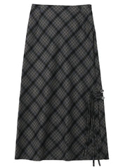 Gonna lunga a quadri neri e grigi, stile scozzese, con dettagli a laccio laterali. Elegante e versatile, perfetta per moda autunno-inverno.