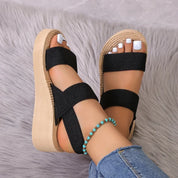Sandali donna con zeppa in sughero, cinturini neri, indossati su tappeto grigio. Accessorio moda estivo, casual, comodo.