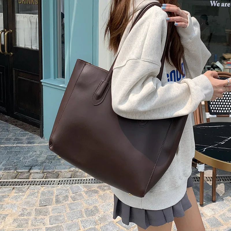 Donna con borsa shopper in pelle marrone, indossa felpa grigia e gonna corta. Moda casual, accessori eleganti, shopping urbano.