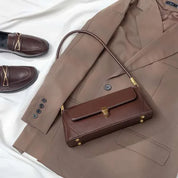Blazer marrone elegante con borsa a tracolla in pelle marrone e mocassini coordinati su sfondo bianco. Moda autunnale, abbigliamento formale.