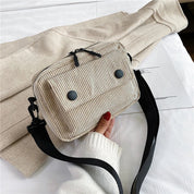 Borsa a tracolla beige in tessuto a coste con tasche frontali e cerniera, manico nero regolabile, su sfondo chiaro. Accessorio moda casual.