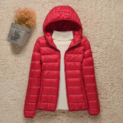 Giacca invernale donna rossa con cappuccio, imbottita, su sfondo beige. Moda femminile, abbigliamento caldo, giacca trapuntata elegante.