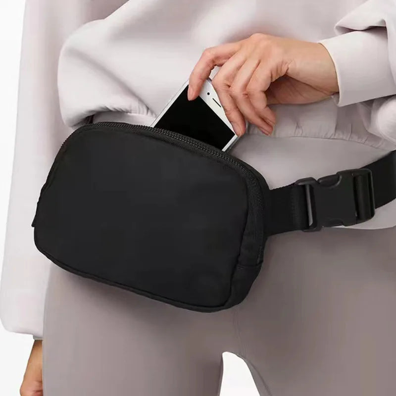 Marsupio nero in tessuto, indossato in vita, con una mano che inserisce uno smartphone. Accessorio moda pratico e versatile per uomo e donna.