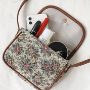 Borsa a tracolla floreale aperta con smartphone, rossetto, cipria e crema. Accessori moda donna, stile vintage, eleganza quotidiana.