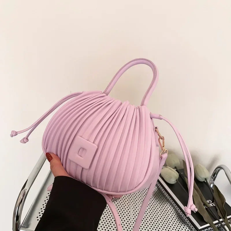 Borsa a mano rosa pastello, design a pieghe, forma rotonda, con manici e tracolla regolabile. Accessorio moda elegante e moderno.