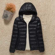 Giacca invernale nera con cappuccio, imbottita e trapuntata, su sfondo beige. Moda donna, abbigliamento caldo, stile casual.