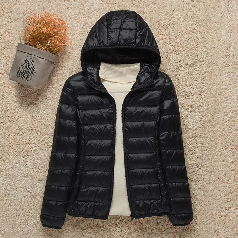 Giacca invernale nera con cappuccio, imbottita e trapuntata, su sfondo beige. Moda donna, abbigliamento caldo, stile casual.