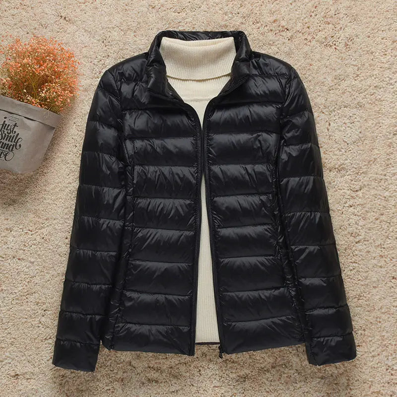 Giacca invernale nera imbottita da donna su sfondo beige, con collo alto e chiusura a zip. Elegante e calda, ideale per la stagione fredda.