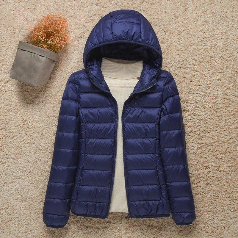Giacca invernale donna blu con cappuccio, imbottita, su sfondo beige. Moda abbigliamento caldo, ideale per freddo. Disponibile online.