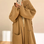 Donna con cappotto lungo in maglia beige, tasche frontali, stile casual chic, perfetto per l'autunno inverno. Fashion femminile elegante.