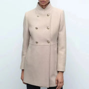 Cappotto donna beige elegante, doppio petto, bottoni dorati, collo alto, tasche laterali. Moda autunno inverno, abbigliamento femminile chic.