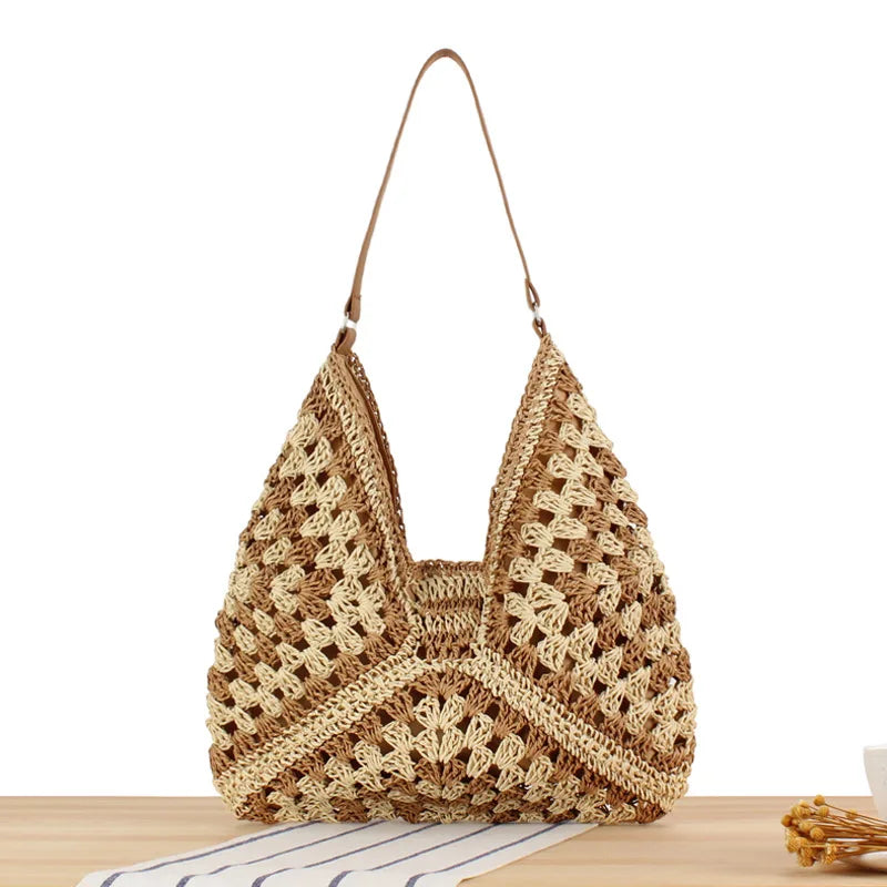 Borsa a tracolla in paglia intrecciata su tavolo di legno, design triangolare, stile boho chic, perfetta per l'estate e la spiaggia.