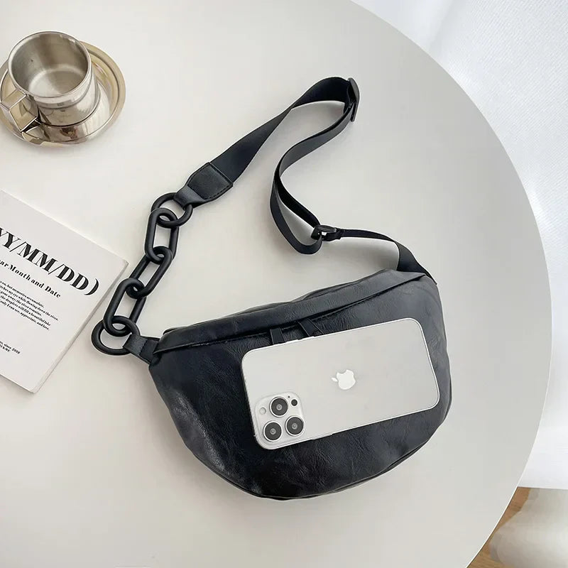 Marsupio in pelle nera su tavolo bianco con smartphone e tazza. Accessorio moda unisex, elegante e pratico per uso quotidiano.