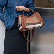 Donna con borsa a tracolla in tessuto a quadri beige e marrone, dettagli in pelle marrone, indossa camicia di jeans e gonna nera. Accessorio moda elegante.