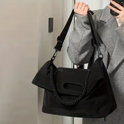 Borsa a tracolla nera elegante, design moderno, manico intrecciato, indossata da persona con cappotto grigio. Accessorio moda versatile.