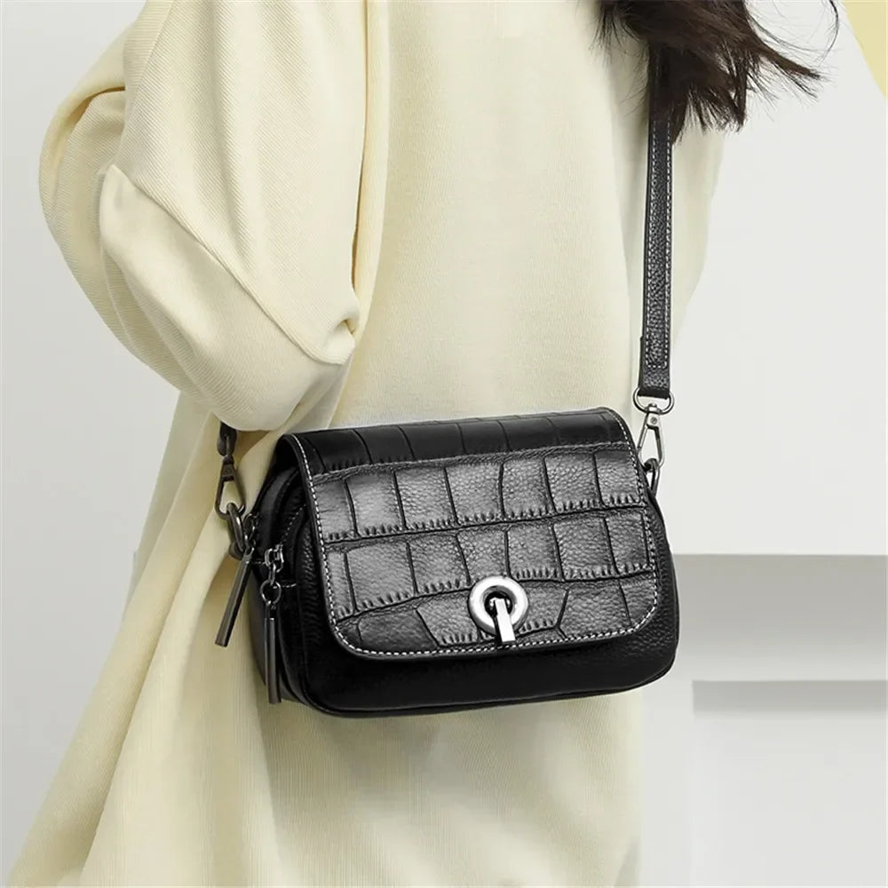 Borsa a tracolla donna in pelle nera con texture coccodrillo, chiusura a gancio, indossata su abito chiaro. Accessorio moda elegante e versatile.